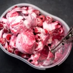 Bac de crème glacée maison à la framboise et marbrée au coulis de framboise, surmontée de framboises entières avec une cuillère à glace
