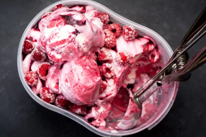Bac de crème glacée maison à la framboise et marbrée au coulis de framboise, surmontée de framboises entières avec une cuillère à glace