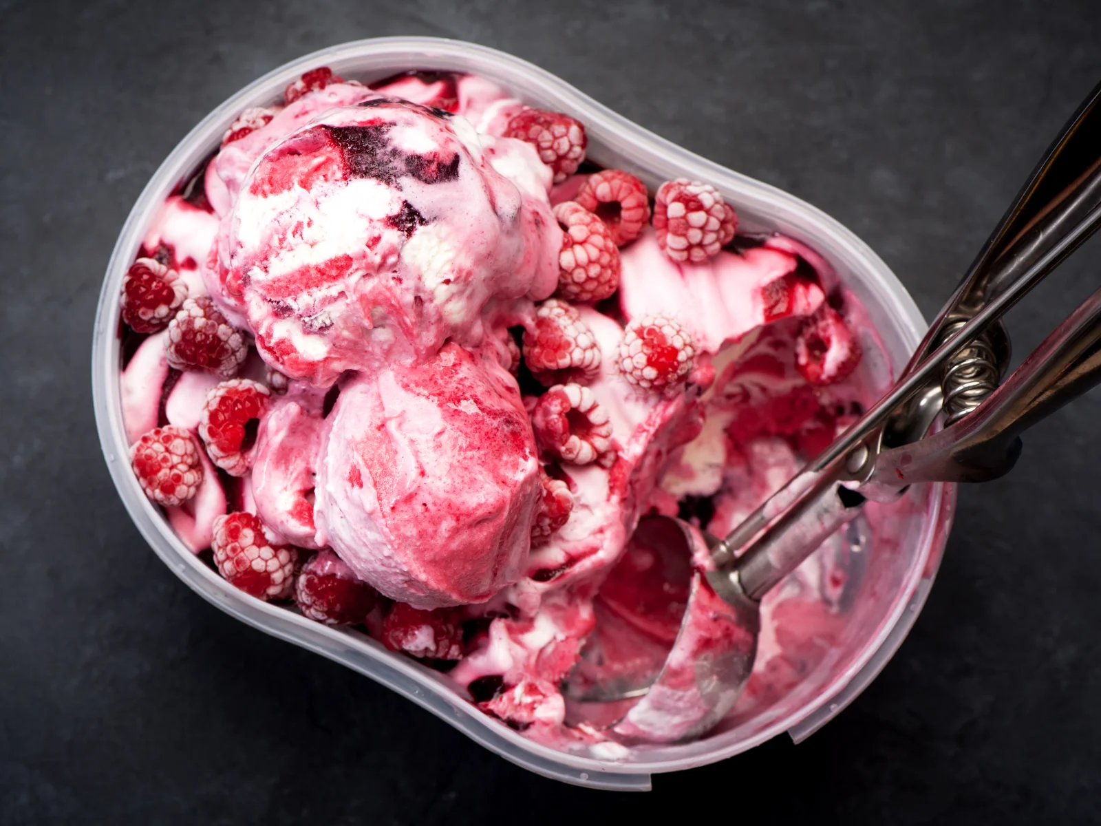 Bac de crème glacée maison à la framboise et marbrée au coulis de framboise, surmontée de framboises entières avec une cuillère à glace